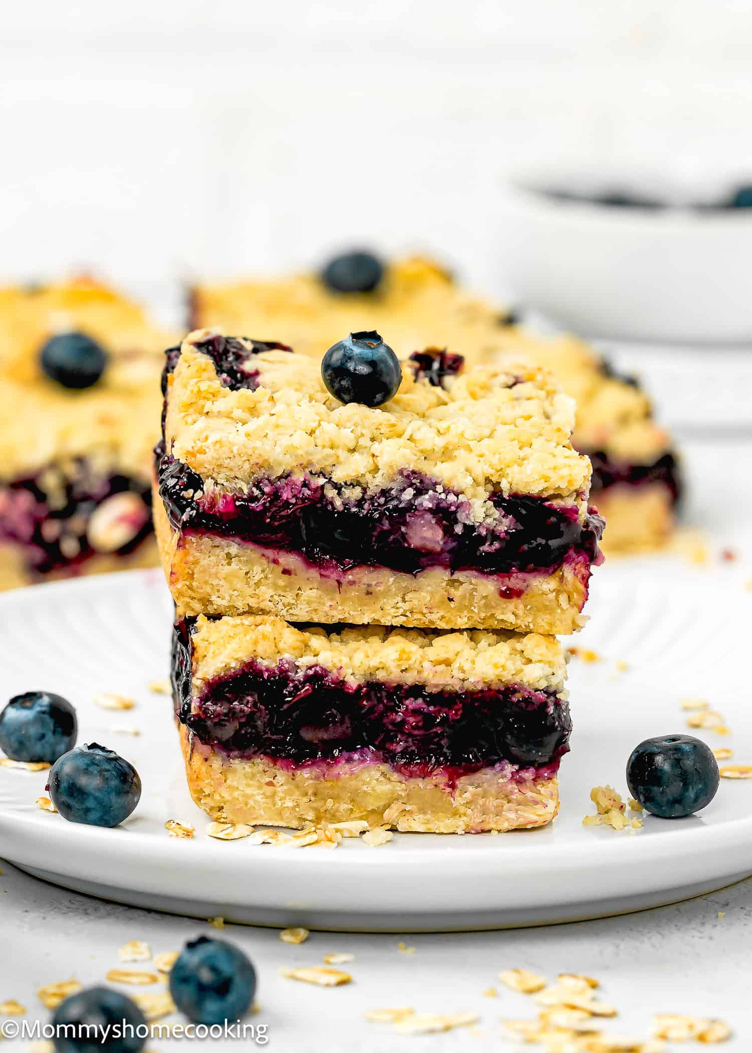 Two easy, eggless blueberry oat crumb bars stacked on a white plate, with oats and fresh blueberries scattered around.