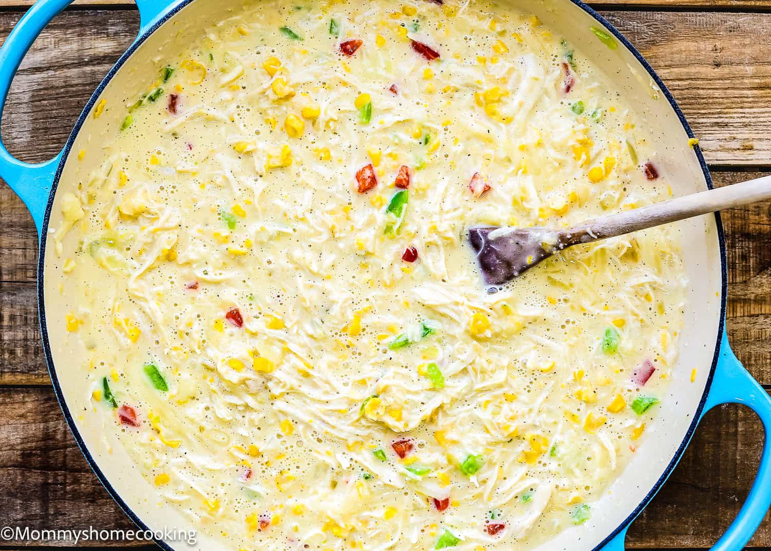 A pot of creamy chicken soup with corn, green and red bell peppers is stirred by a wooden spoon. This dish, similar to Easy Green Chicken Enchiladas, offers a comforting blend of flavors perfect for any cozy night in.
