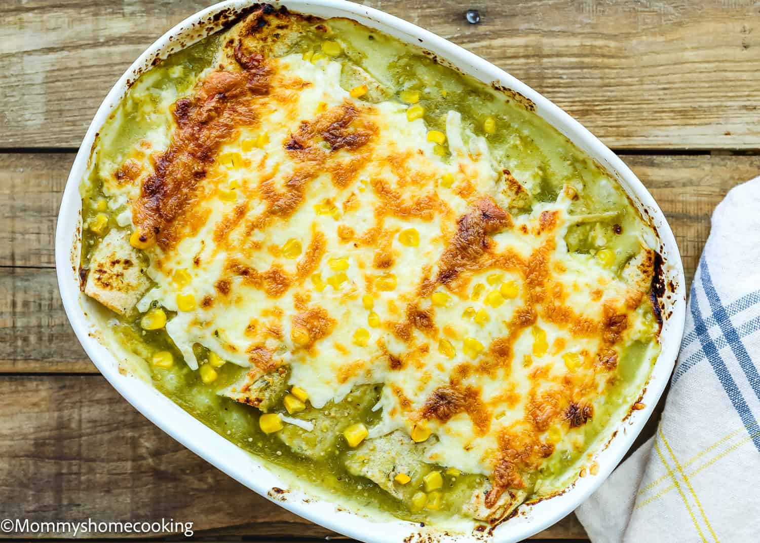 Easy Green Chicken Enchiladas are a delicious baked dish featuring enchiladas covered in melted cheese and green sauce, garnished with corn. They're perfectly presented in a white oval dish on a wooden table.