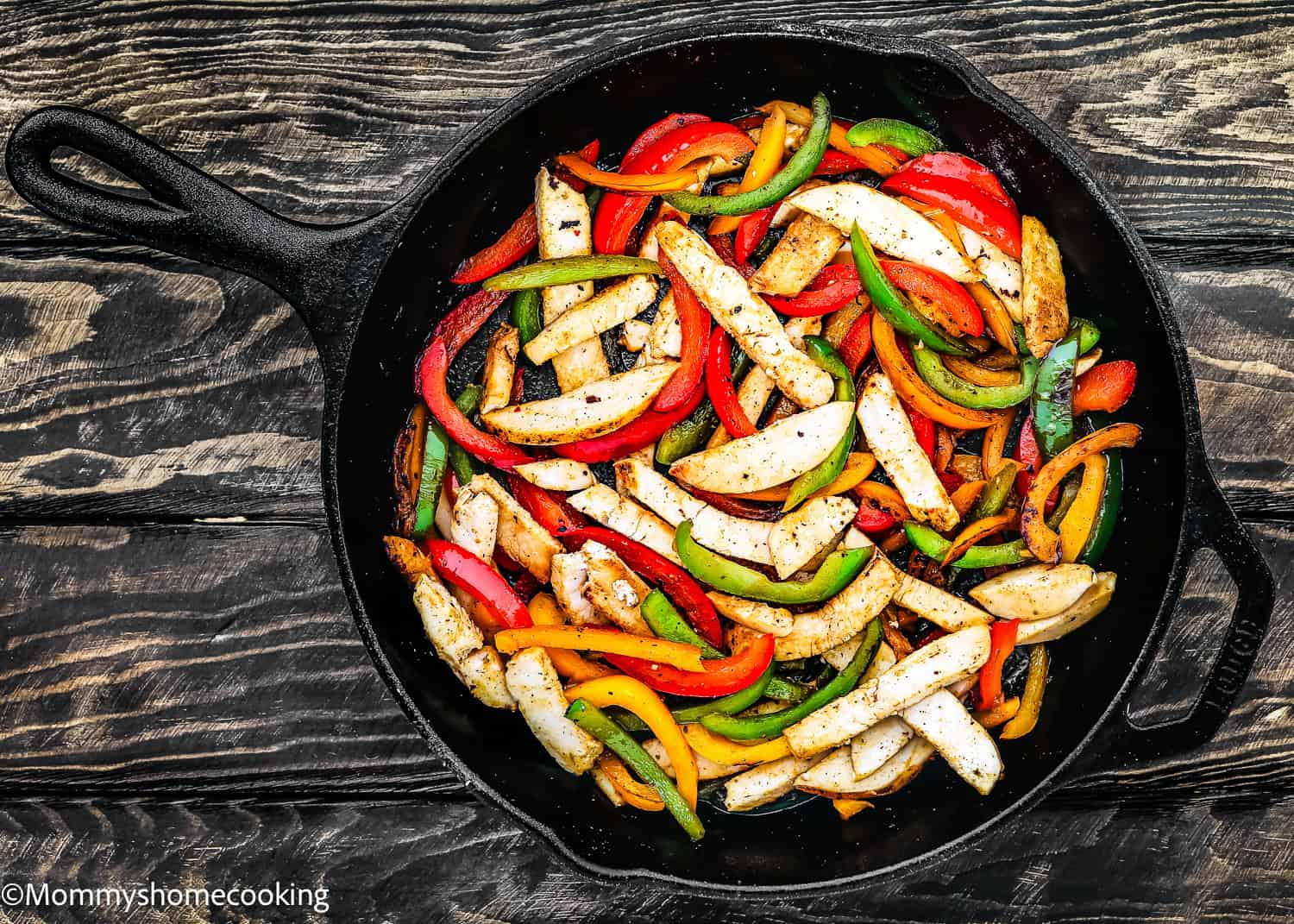 A skillet with cooked chicken strips, red, green, and yellow bell peppers sits on a rustic wooden surface, perfect for transforming into an easy turkey fajita bowl.