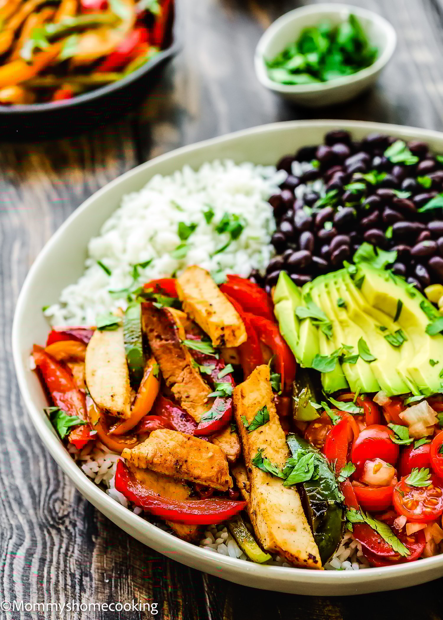 An easy turkey fajita bowl featuring grilled chicken strips, a medley of vibrant red and green peppers, creamy avocado, black beans, and rice topped with chopped tomatoes and fresh cilantro. This colorful dish is beautifully presented on a wooden table.