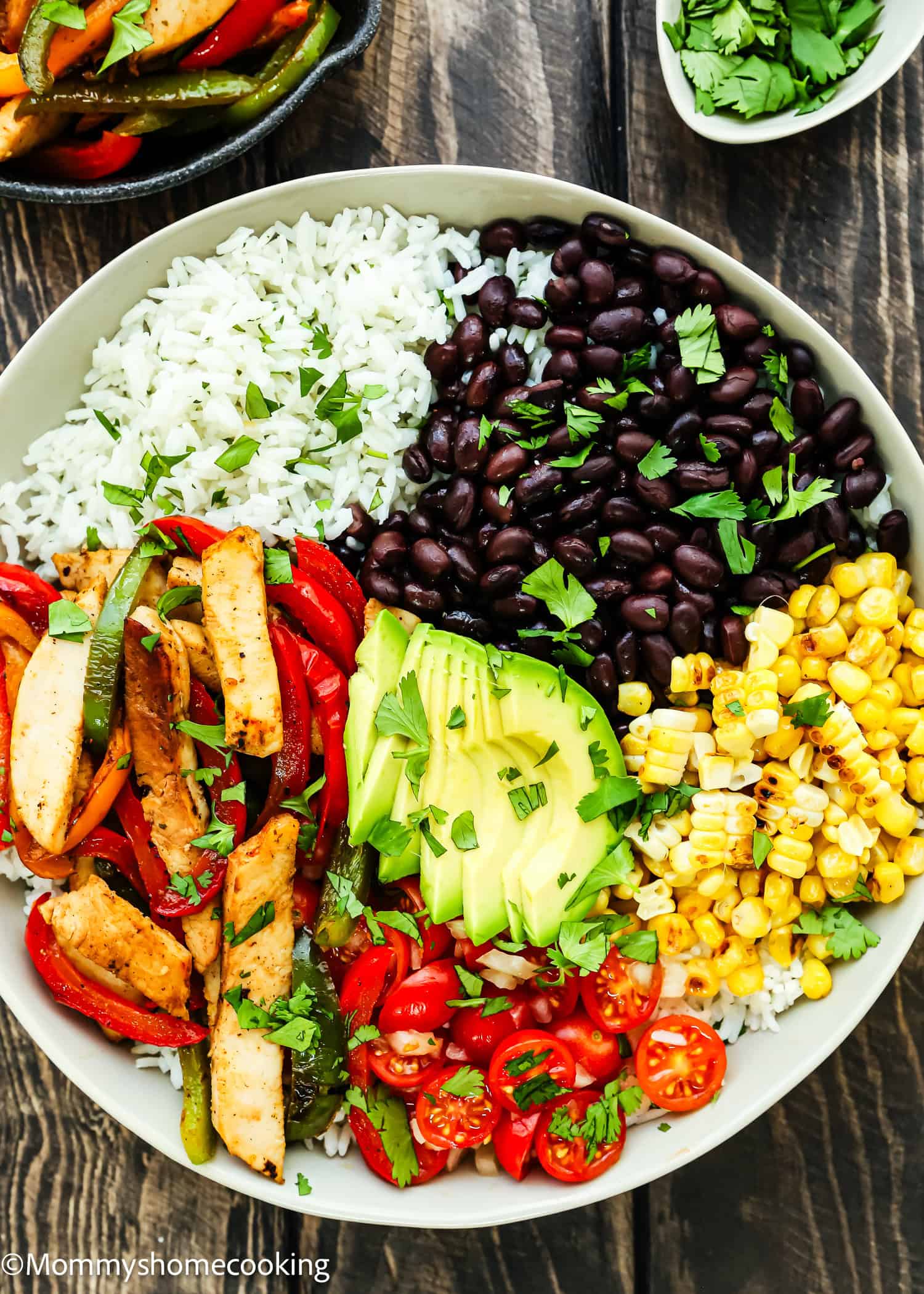 An Easy Turkey Fajita Bowl, featuring rice, black beans, corn, succulent grilled chicken, bell peppers, creamy avocado slices, cherry tomatoes, and fresh cilantro sits invitingly on a wooden table.