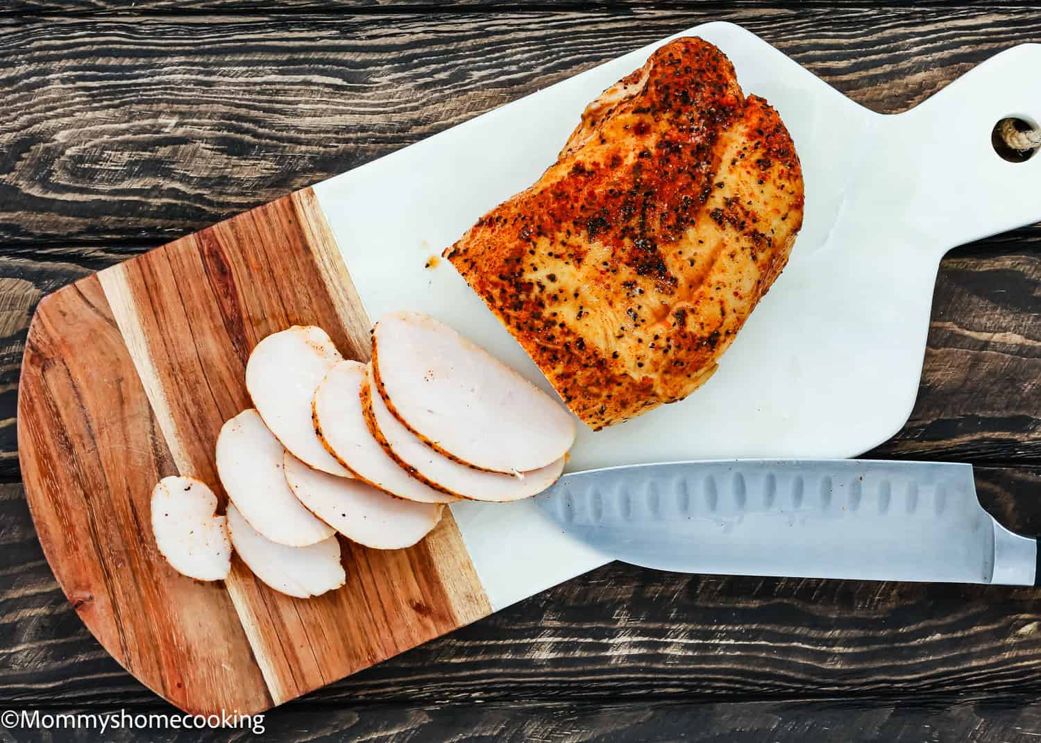 Sliced roasted chicken breast on a wooden cutting board with a white handle, accompanied by a knife, set on a textured dark surface. Perfect for crafting an easy turkey fajita bowl to enjoy at any meal.
