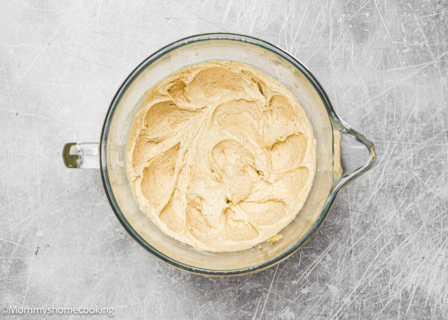 A bowl of light brown, creamy peanut butter frosting sits on a gray textured surface, perfectly complementing the flavors of eggless brown butter Snickerdoodle cookies.