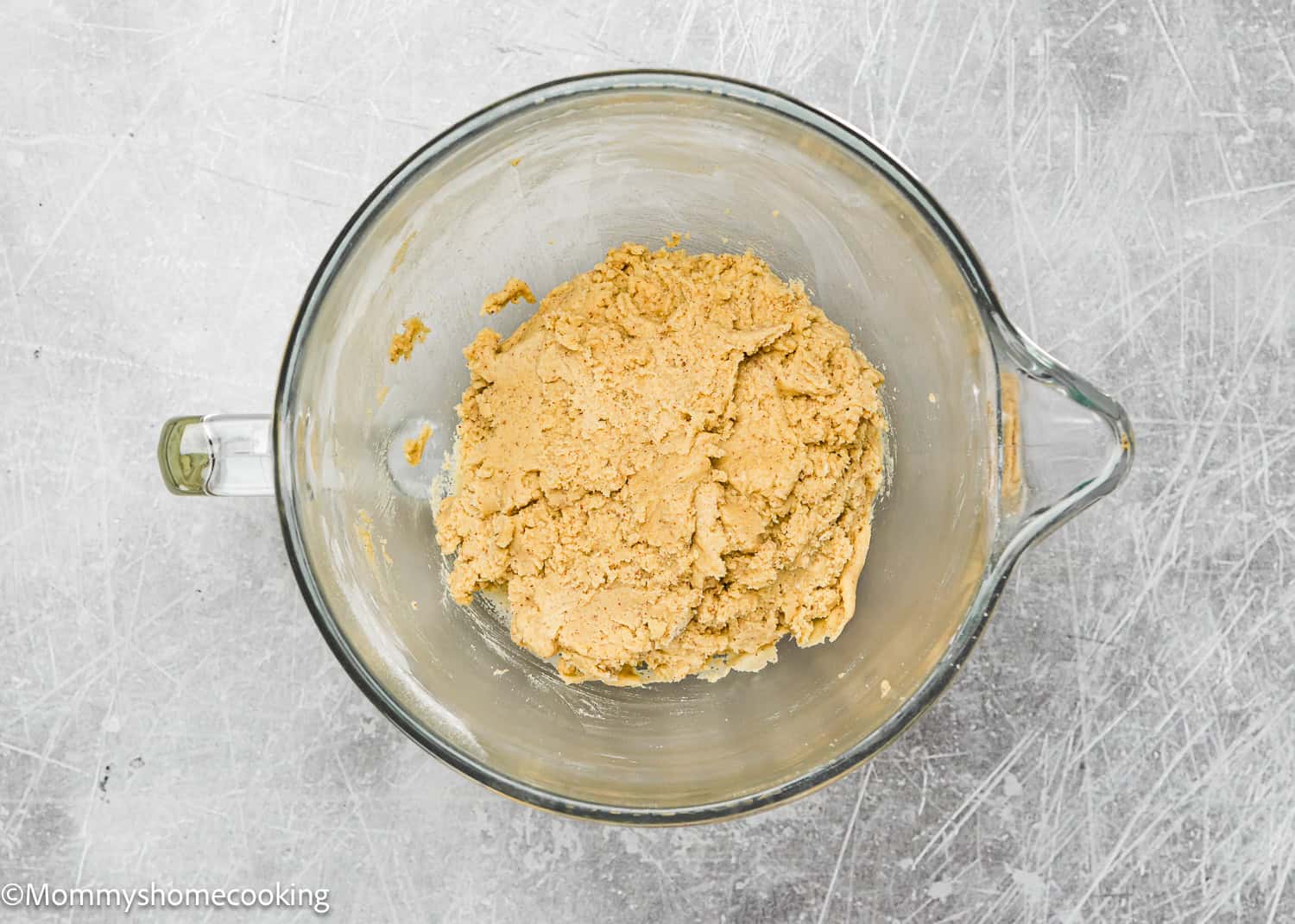 A glass bowl filled with eggless brown butter snickerdoodle cookie dough sits on a scratched gray surface.