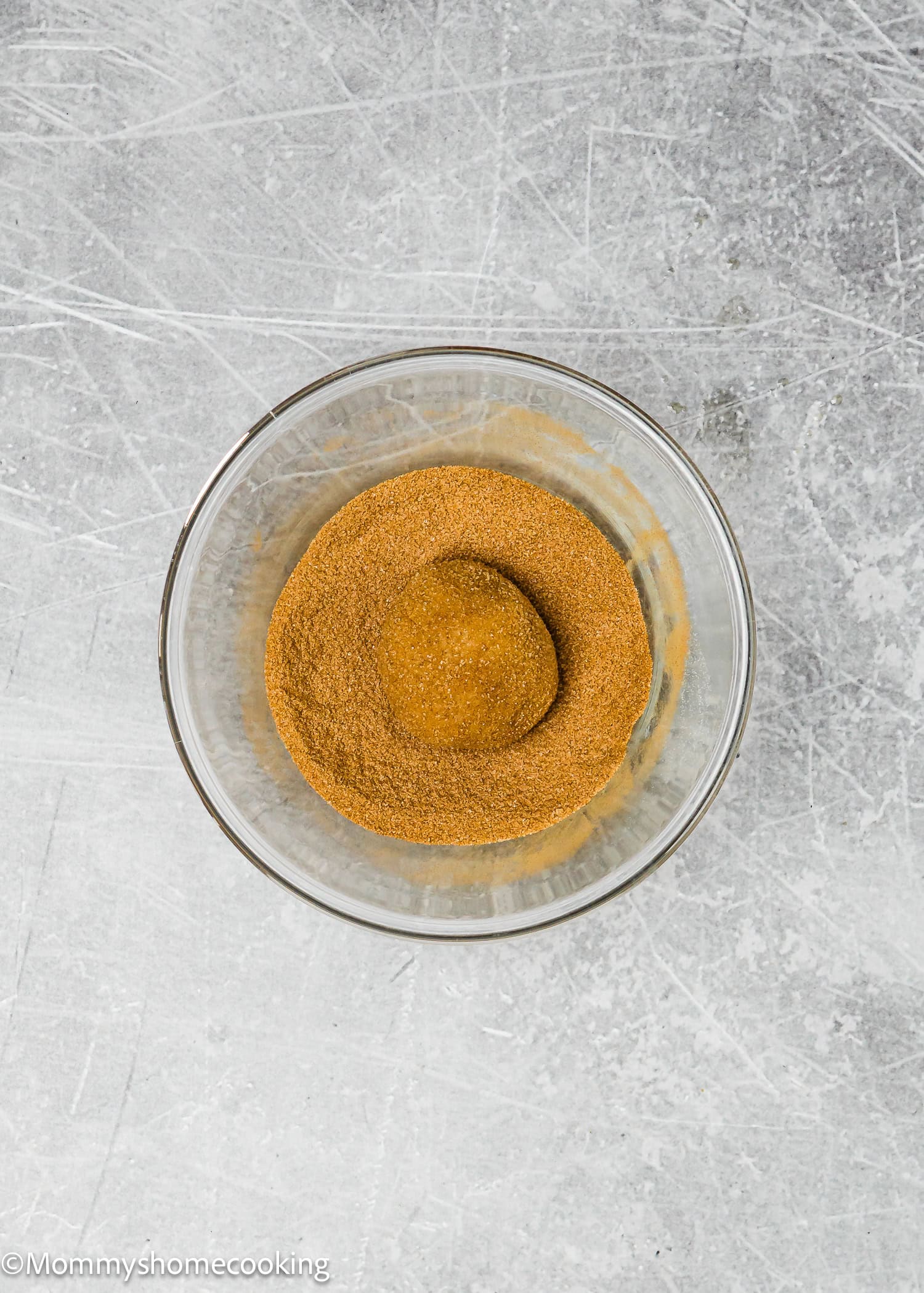 A glass bowl filled with light brown powder sits on a textured gray surface, ready for crafting delicious eggless brown butter snickerdoodle cookies.