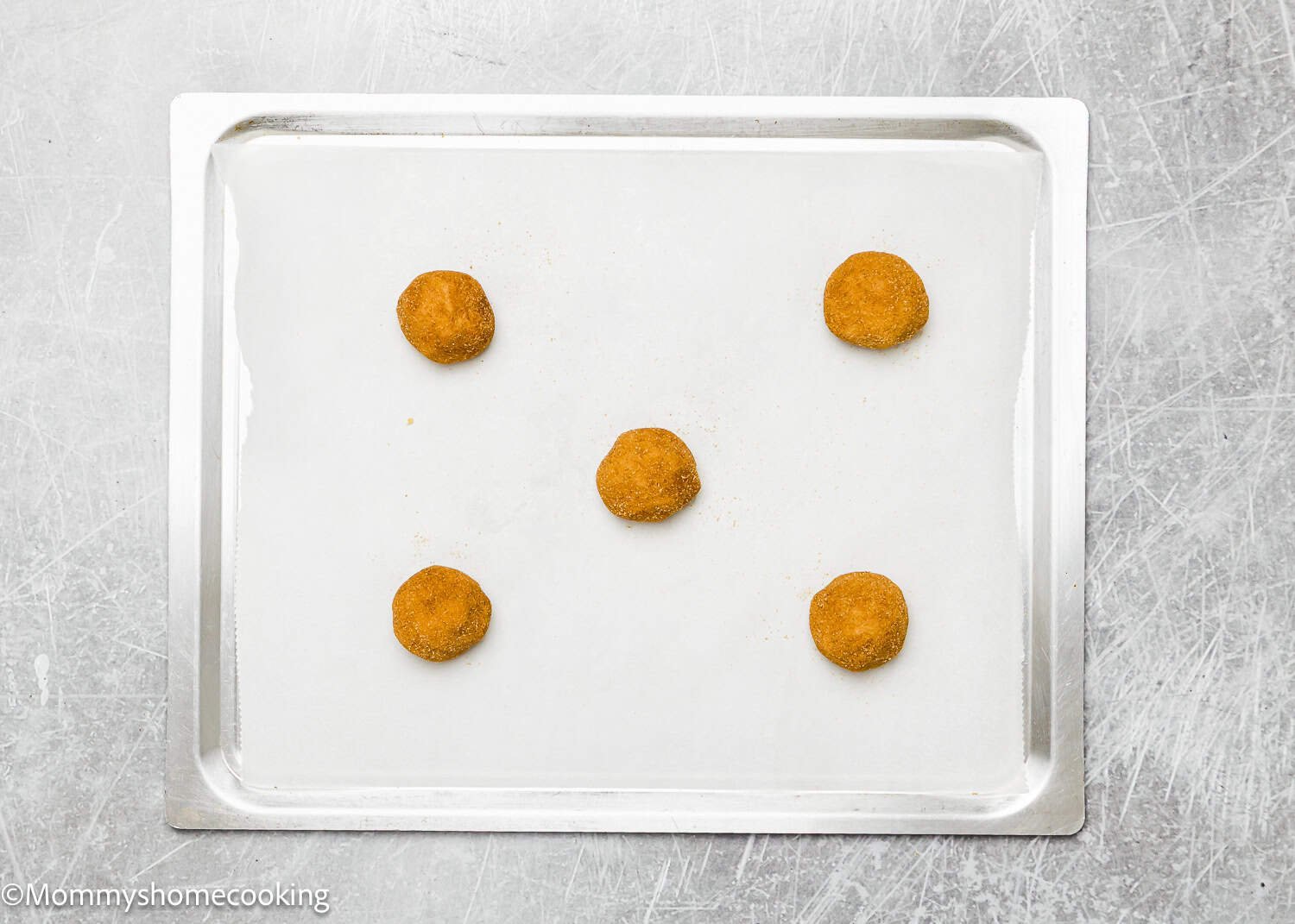 Five uncooked eggless brown butter snickerdoodle cookie dough balls sit on a parchment-lined baking sheet.