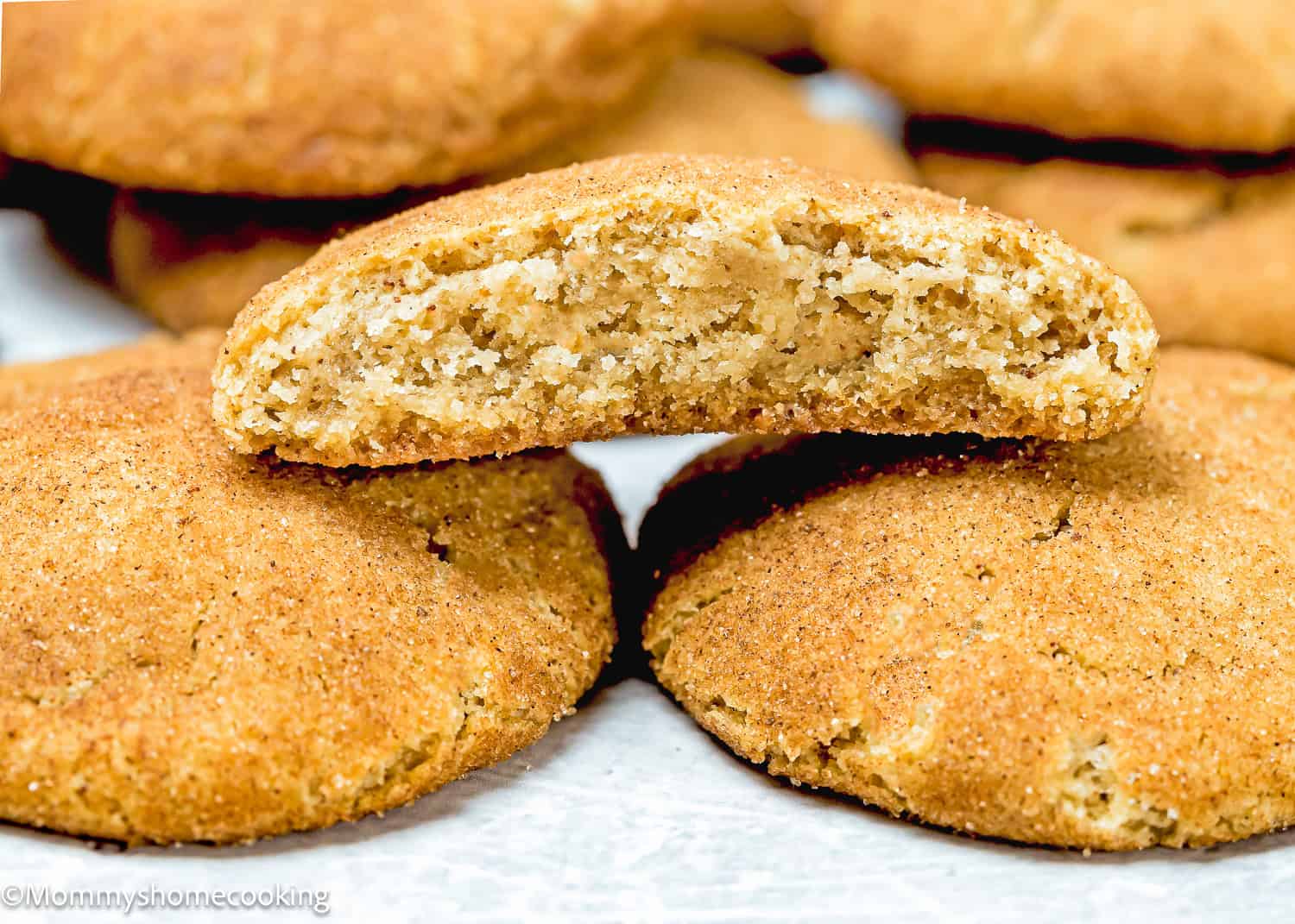 Close-up of several Eggless Brown Butter Snickerdoodle Cookies with one cut in half to display the interior texture. They are dusted with cinnamon sugar.