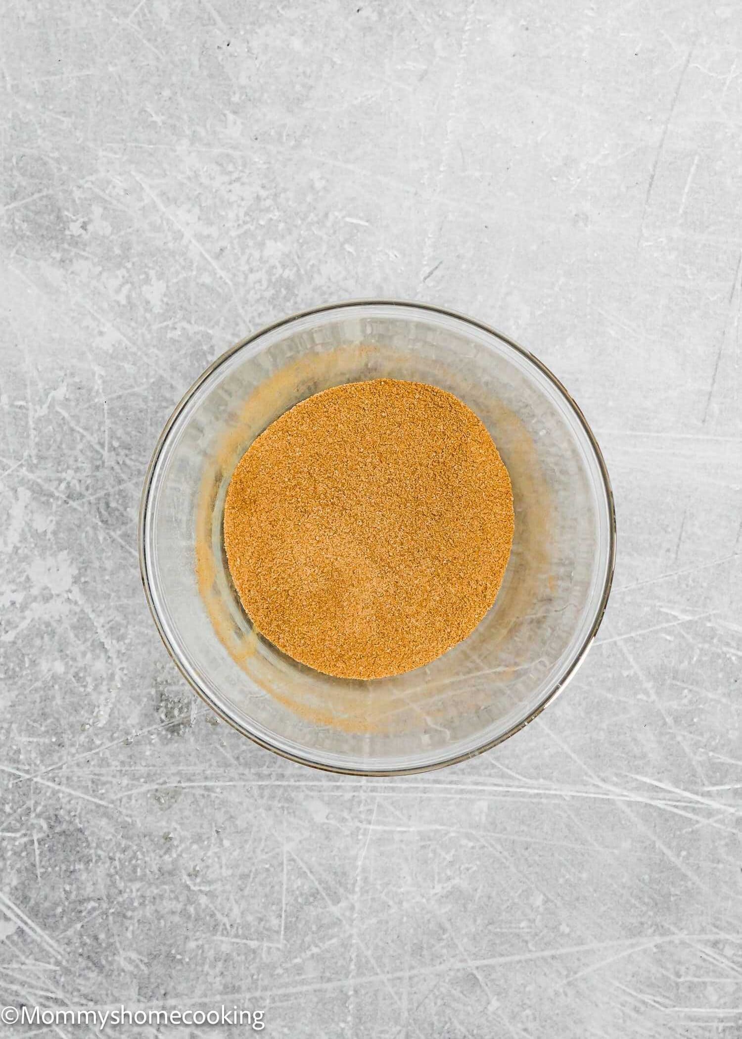 A glass bowl filled with fine brown powder sits on a textured gray surface, ready to be turned into delicious eggless brown butter snickerdoodle cookies.