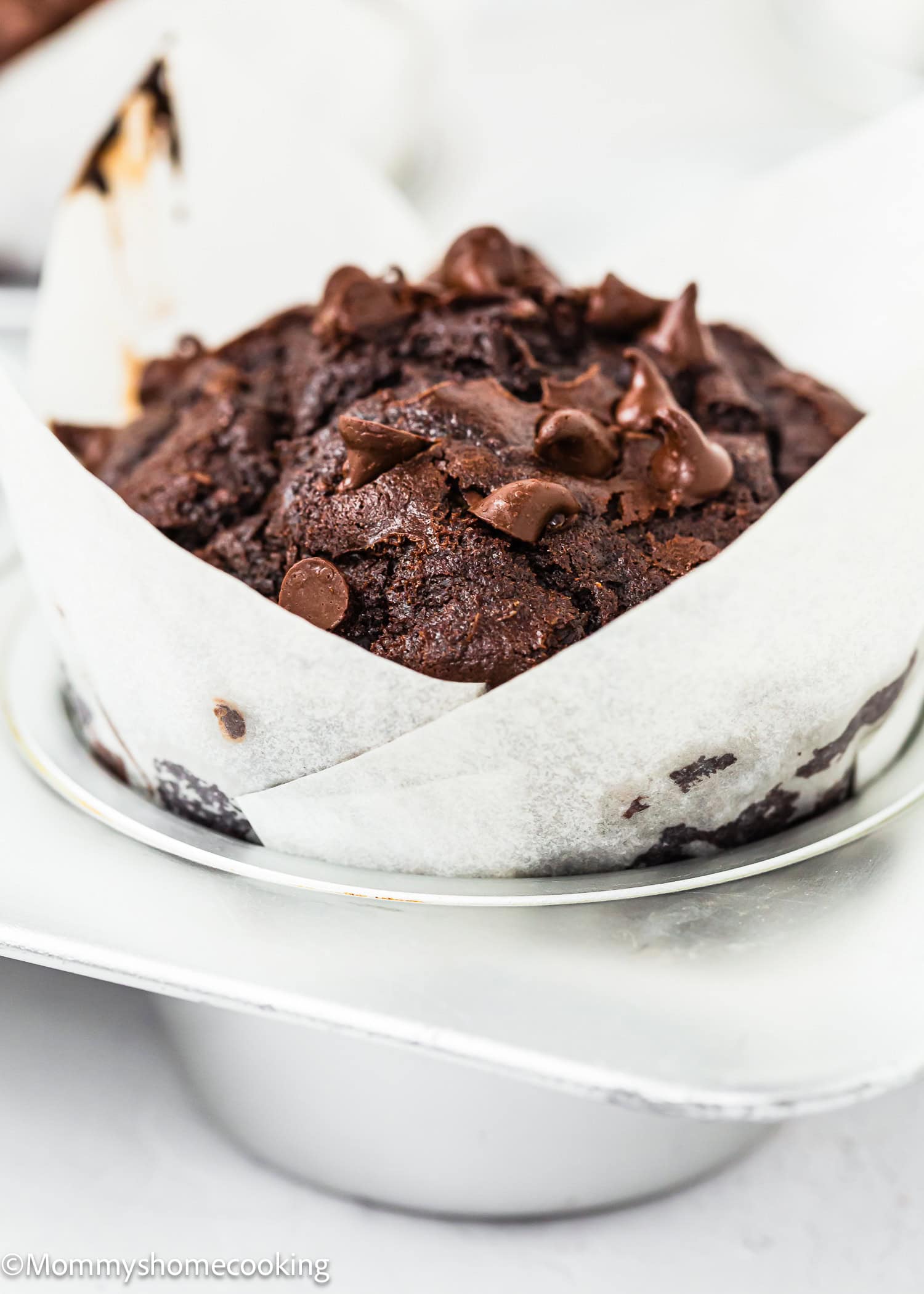 Eggless chocolate zucchini muffin with chocolate chips in a white paper liner, resting in a metallic muffin tray.