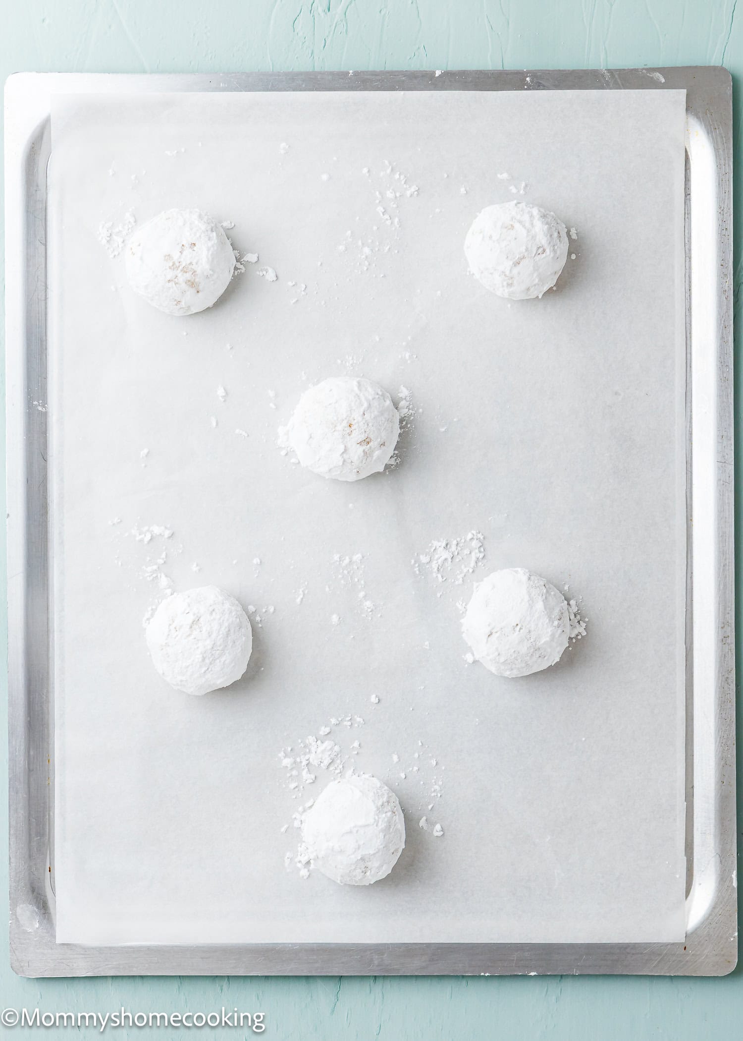 Six eggless lemon crinkle cookies are dusted with powdered sugar and arranged on a parchment-lined baking sheet.