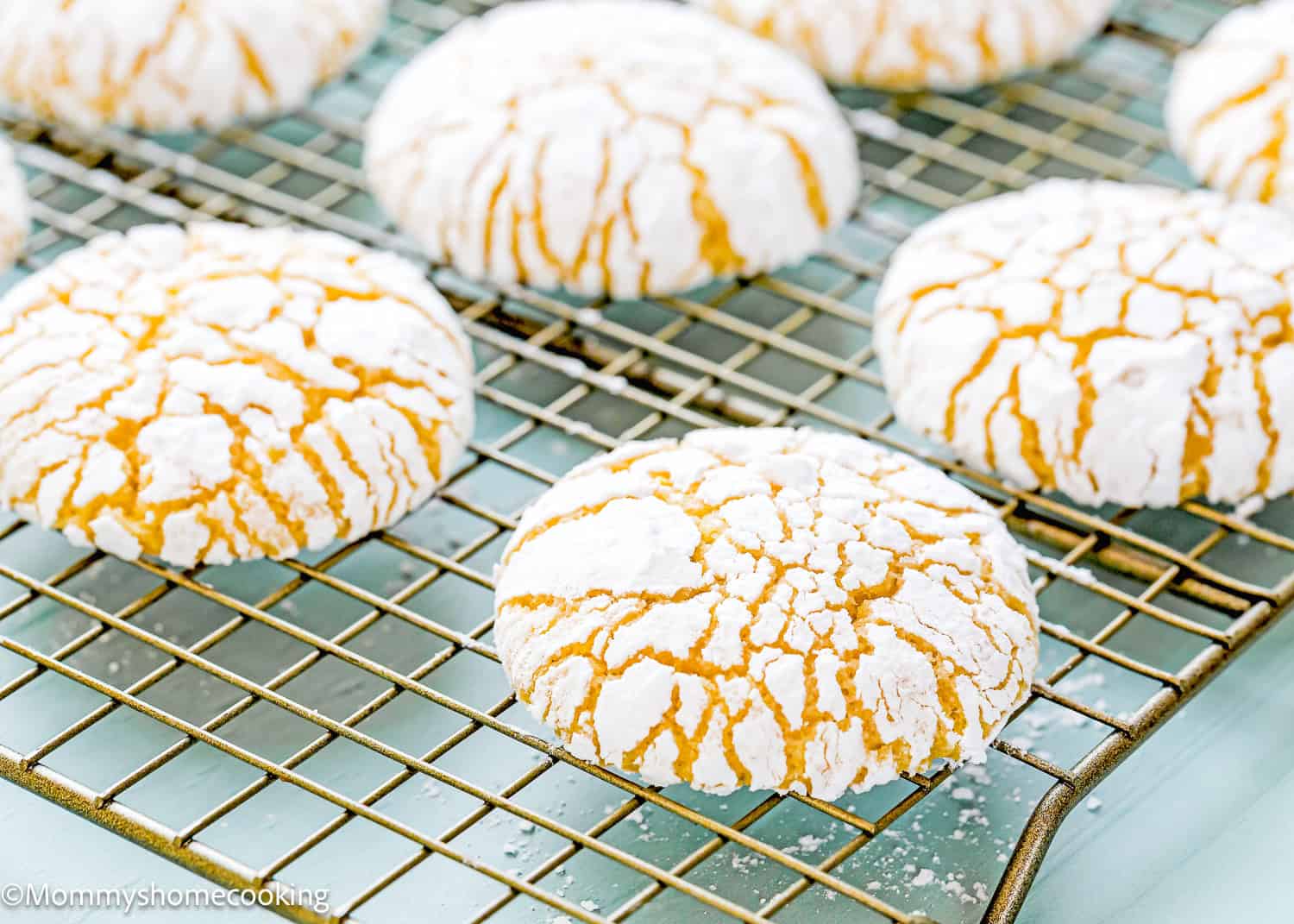 Eggless lemon crinkle cookies dusted in powdered sugar cooling on a wire rack.