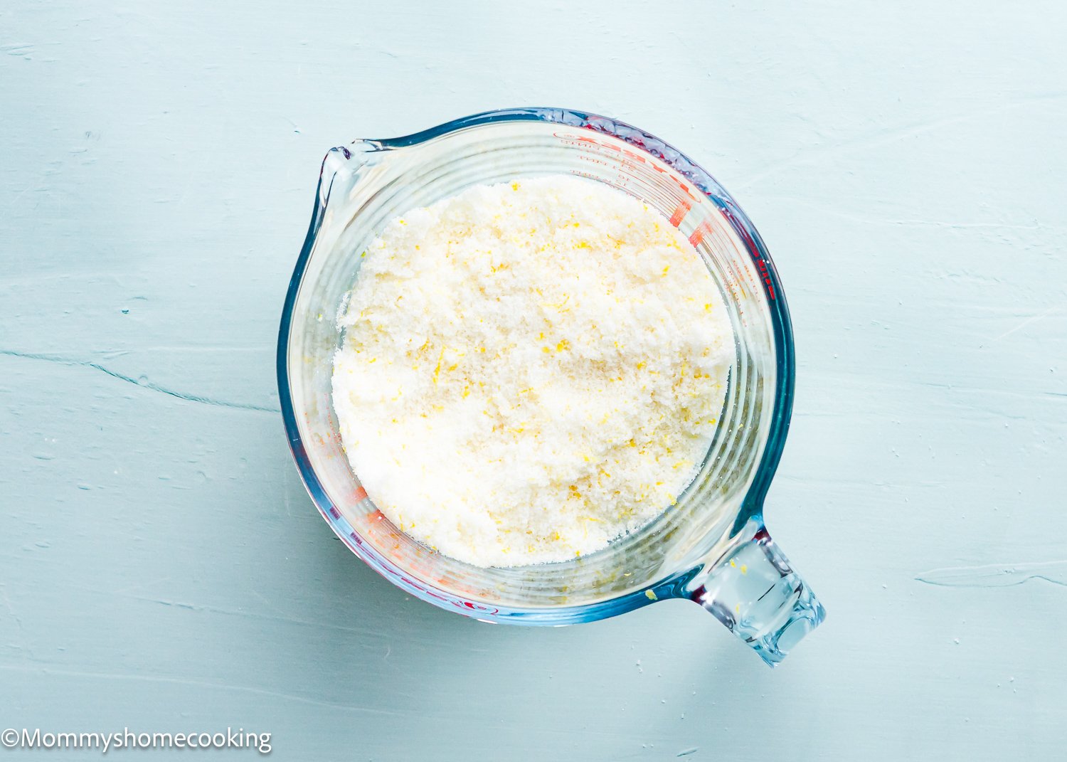 A glass measuring cup filled with granulated sugar, perfect for baking eggless lemon crinkle cookies.