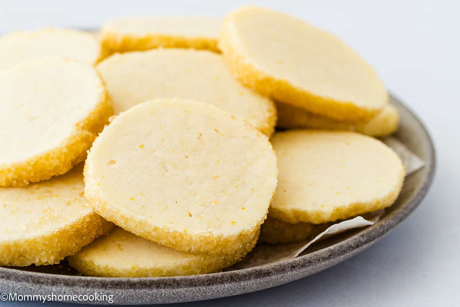 A plate of round, light-colored Eggless Lemon Slice and Bake Cookies stacked in layers against a light background.