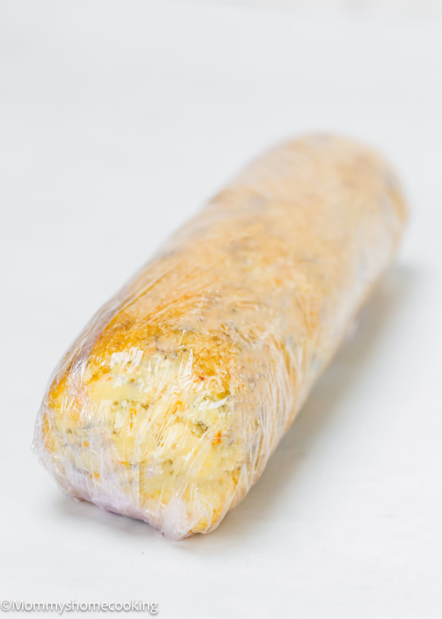 A loaf of bread, reminiscent of the simplicity of eggless lemon slice and bake cookies, is wrapped in clear plastic wrap and rests elegantly on a white surface.