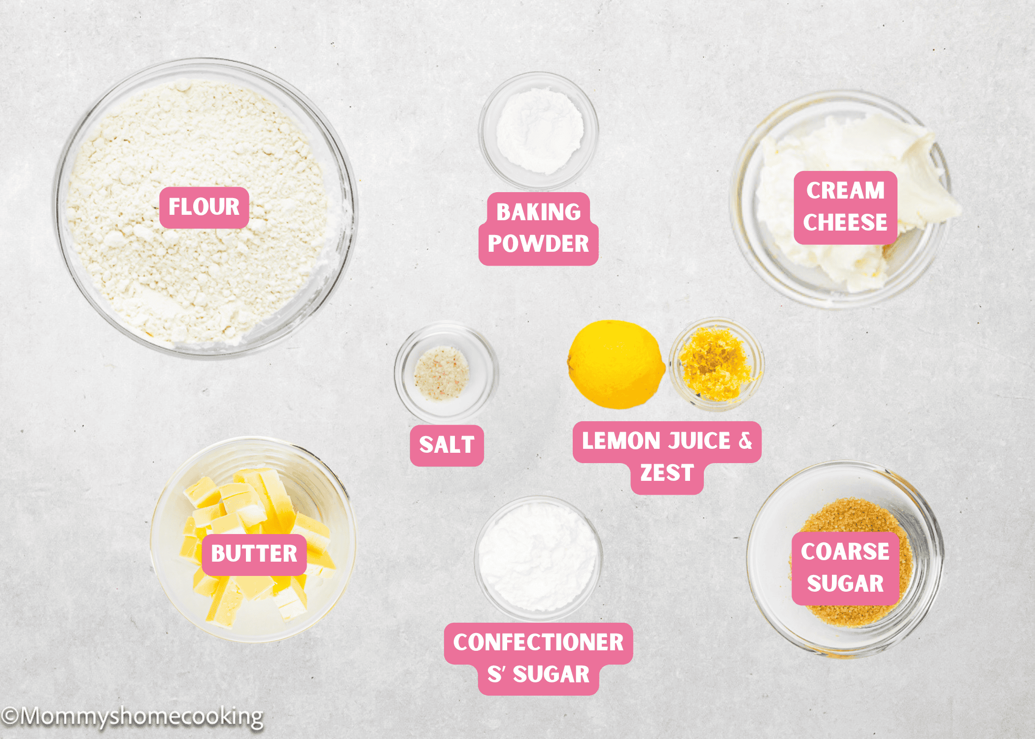 Various baking ingredients for Eggless Lemon Slice and Bake Cookies are in labeled glass bowls on a light surface, including flour, butter, cream cheese, baking powder, salt, lemon juice and zest, confectioners' sugar, and coarse sugar.