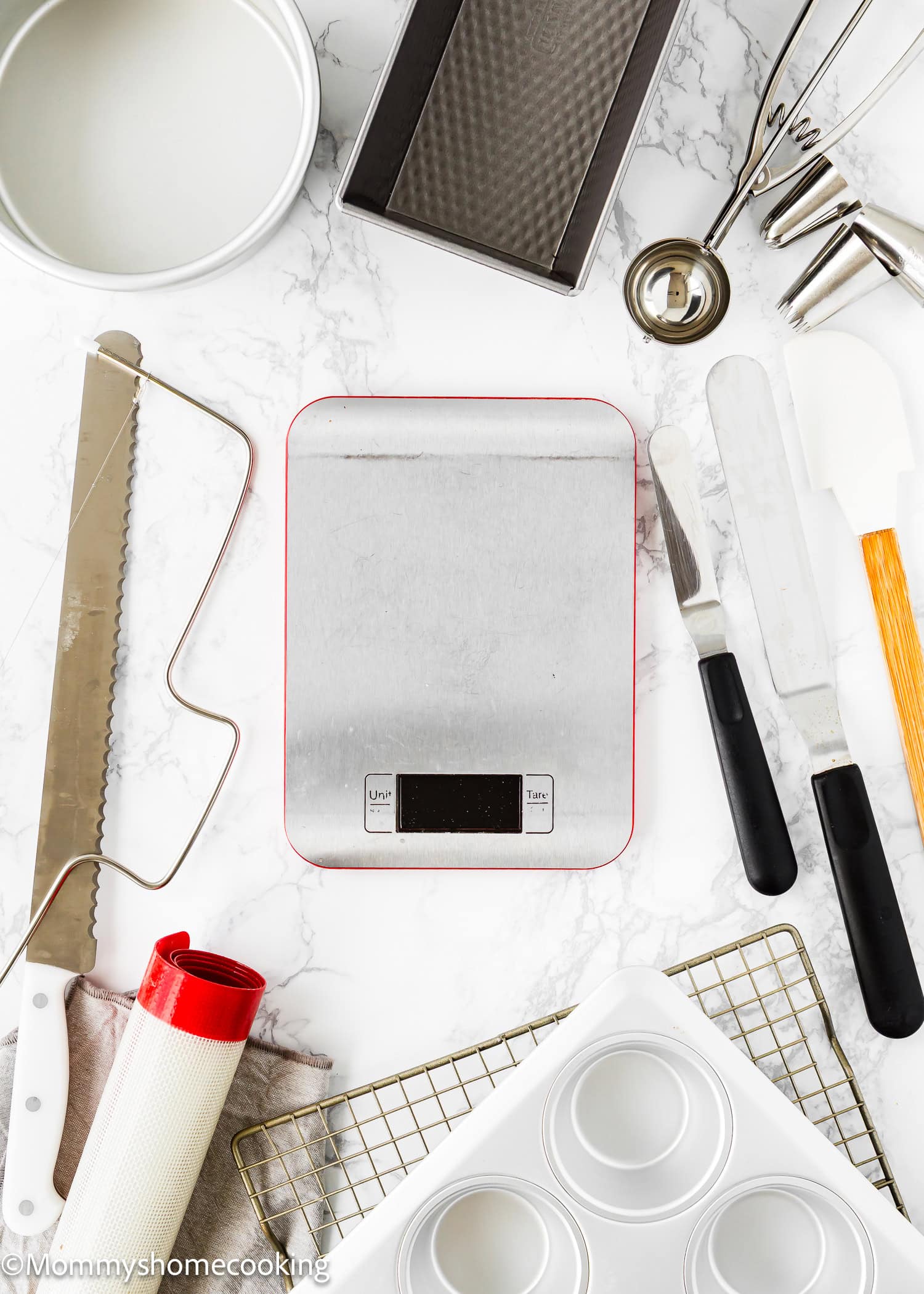 A curated collection of essential tools for egg-free baking is artfully arranged on a marble surface, all centered around a digital kitchen scale.