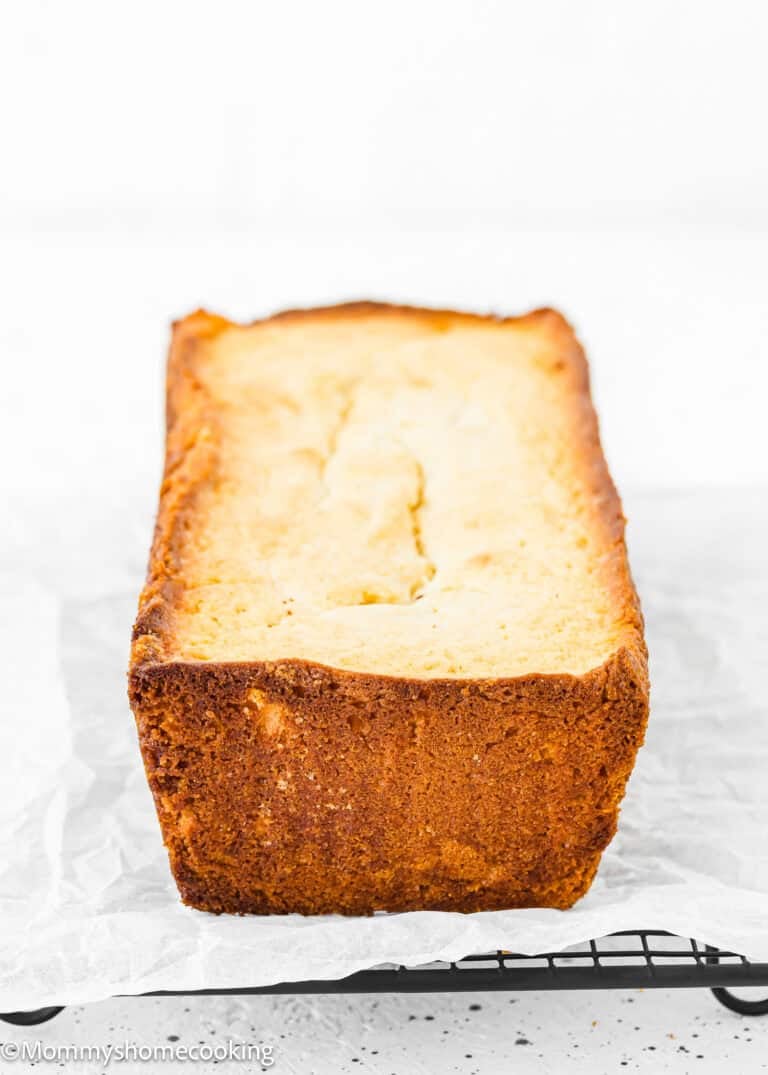 A loaf of freshly baked bread with a golden-brown crust sits on a cooling rack lined with parchment paper, showcasing the success of troubleshooting egg-free baking to perfection.