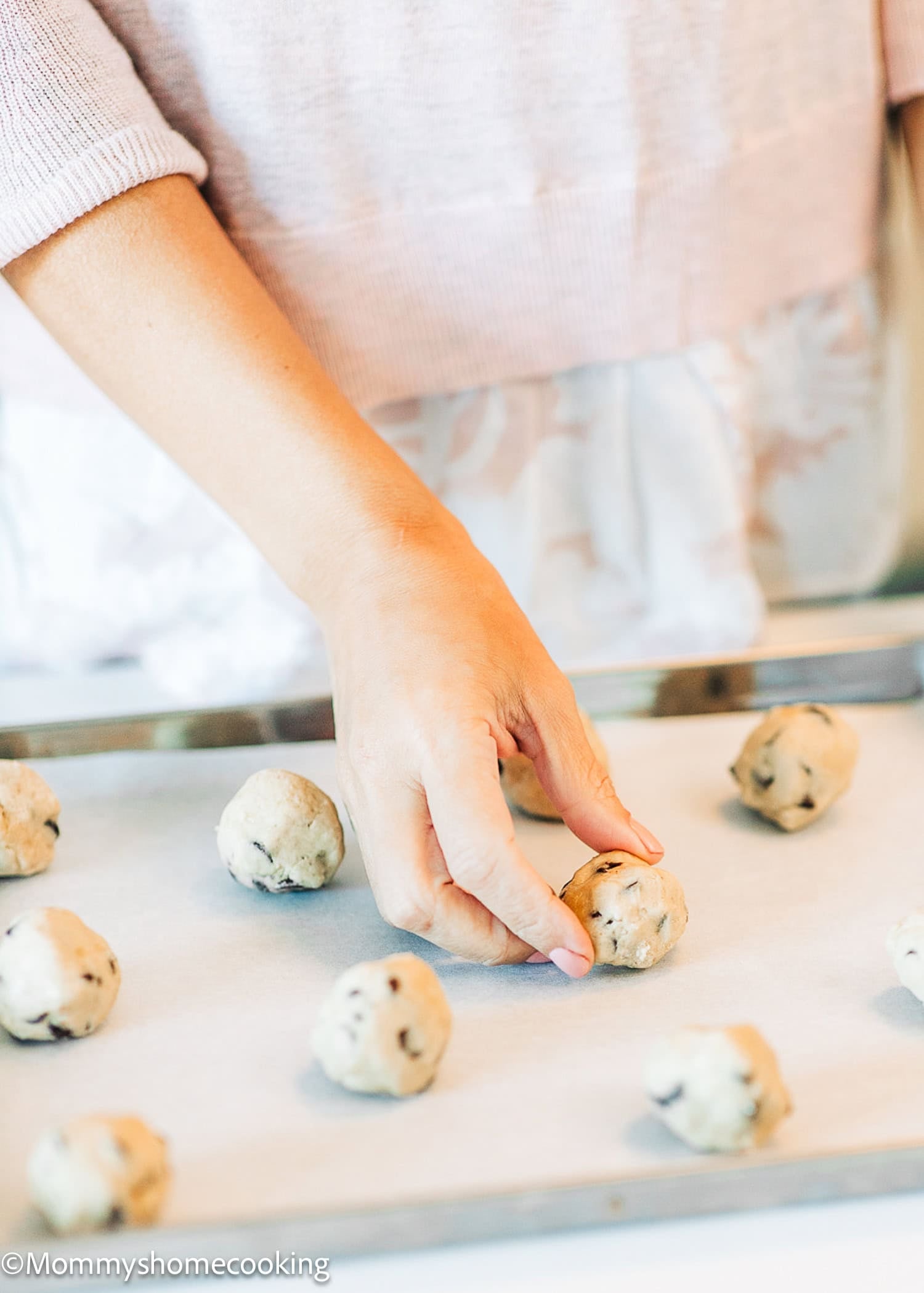 A person places a ball of chocolate chip cookie dough onto a parchment-lined baking sheet among other dough balls, reflecting on the 7 Things I Wish I Knew When Starting Egg-Free Baking.