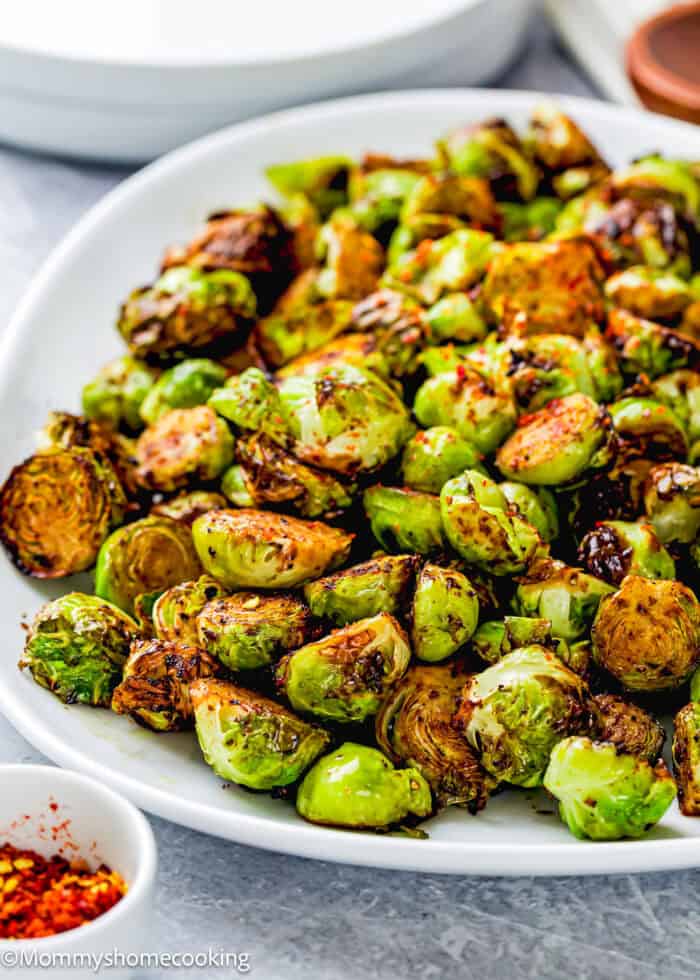 A white plate of roasted Brussels sprouts, lightly browned and perfectly crisped in the air fryer, garnished with red pepper flakes.