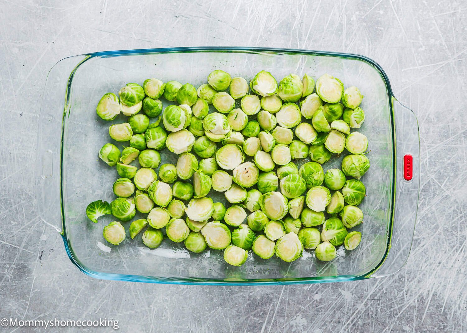 Glass baking dish filled with air fryer Brussels sprouts on a textured gray surface.