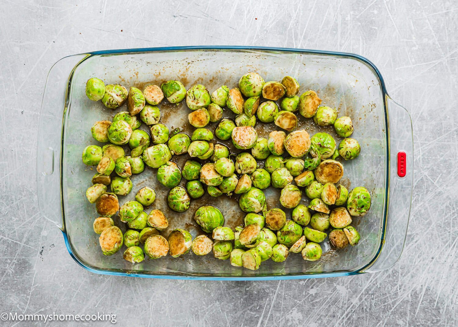 Air fry Brussels sprouts halves in a glass baking dish on a scratched metal surface for a crispy, flavorful side dish.