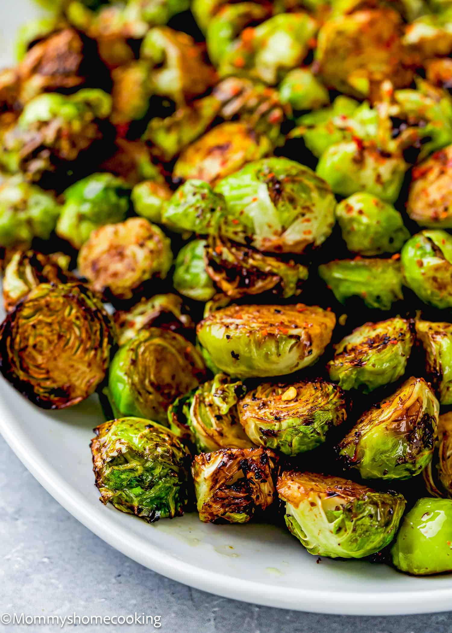 A close-up of air-fried Brussels sprouts on a white plate, lightly charred and seasoned with red pepper flakes.