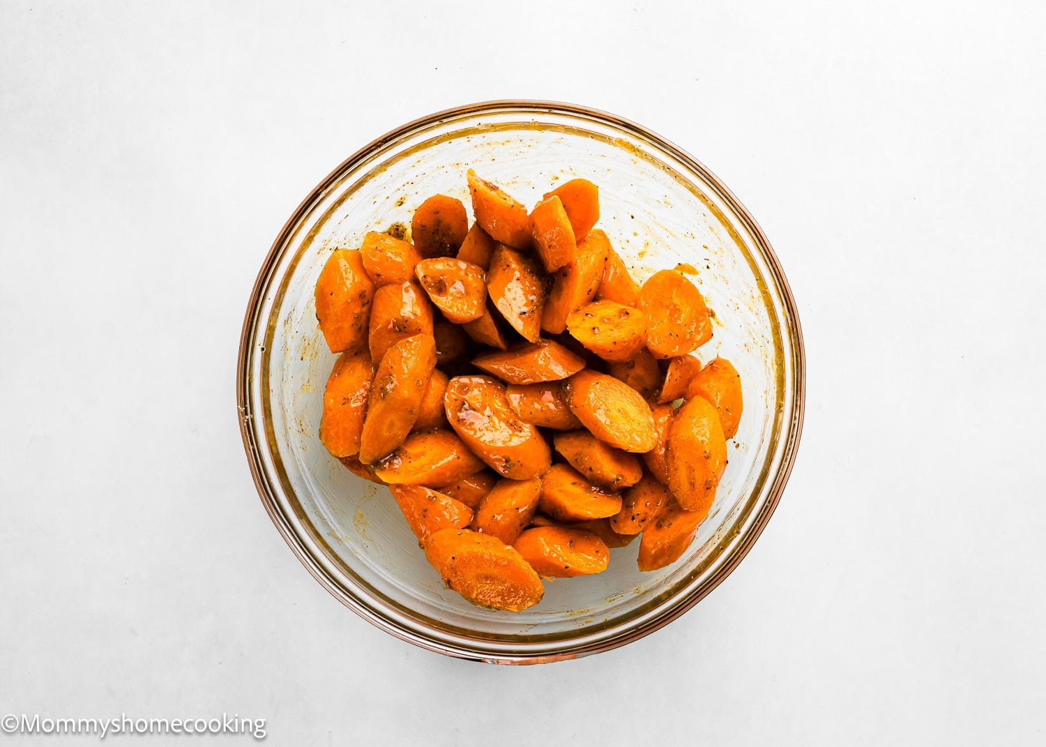 A glass bowl filled with Air Fryer Honey Glazed Carrots, coated in spices and seasoning, placed on a white surface.
