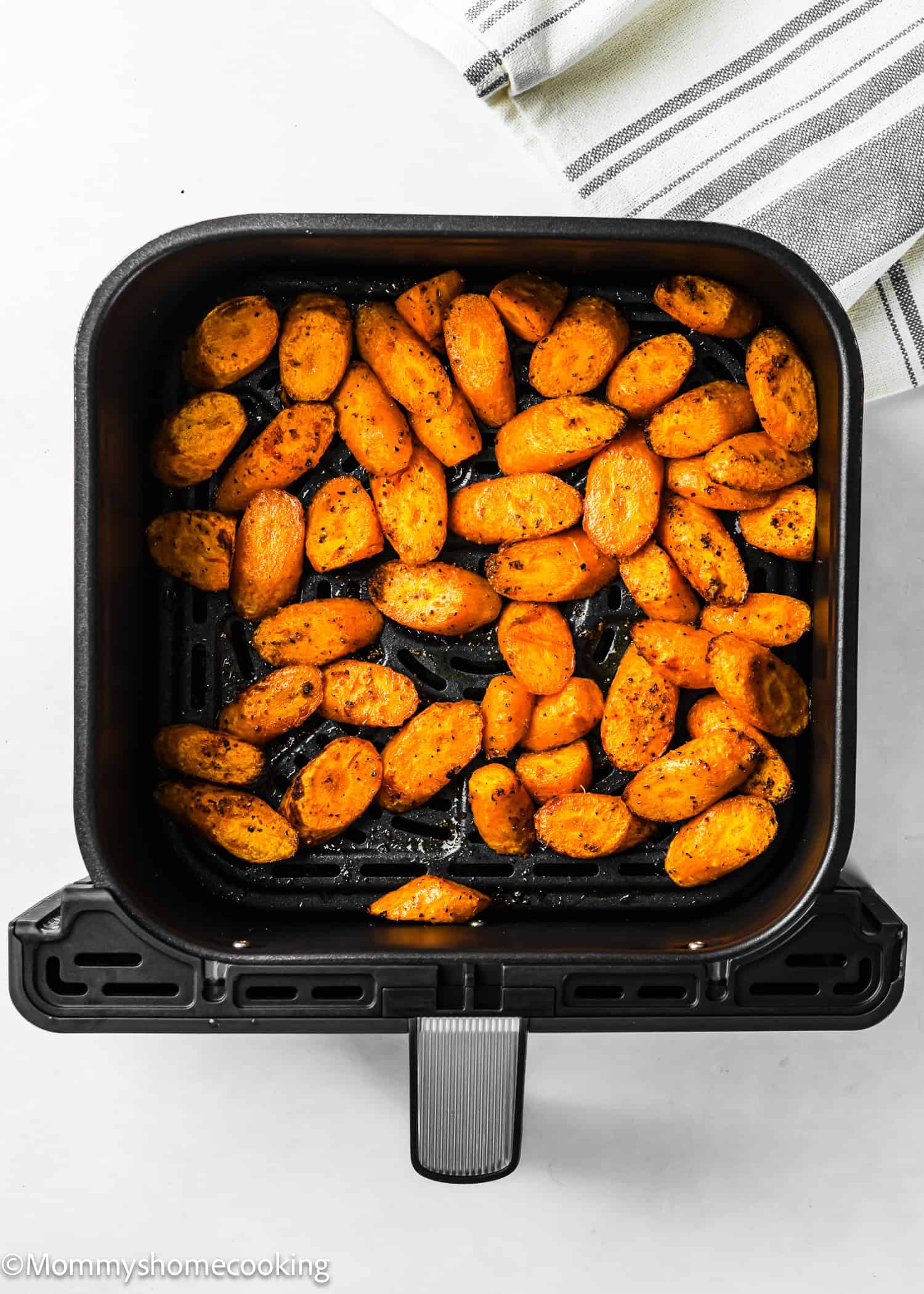 Air fryer basket filled with Air Fryer Honey Glazed Carrots, roasted and seasoned, viewed from above on a white surface with a striped cloth in the background.