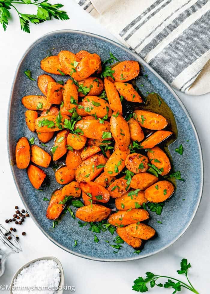 Air Fryer Honey Glazed Carrots roasted and garnished with chopped parsley, served on an oval gray plate with a striped napkin, salt, and pepper on the side.