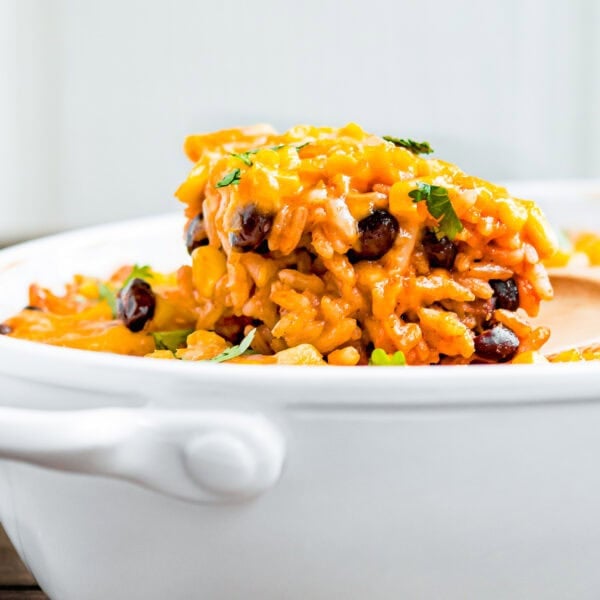 A serving of Cheesy Enchilada Rice and Beans Casserole with black beans and corn in a white ceramic dish, garnished with chopped herbs.