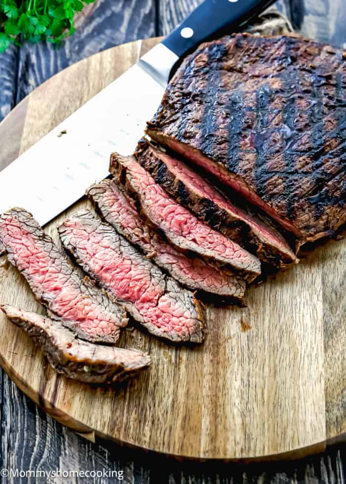 Easy Carne Asada with the best marinade ever—sliced grilled steak with a seared exterior and pink center is arranged on a wooden cutting board beside a large knife.