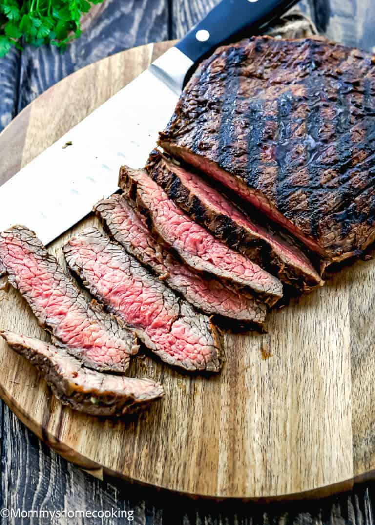Easy Carne Asada with the best marinade ever—sliced grilled steak with a seared exterior and pink center is arranged on a wooden cutting board beside a large knife.