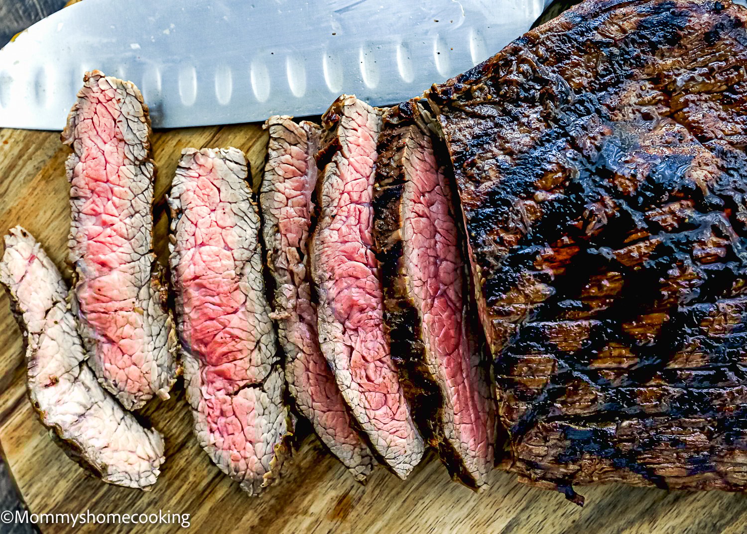 Easy Carne Asada with the best marinade ever—sliced grilled steak on a wooden cutting board, showing a pink interior, with a large knife placed above the meat.