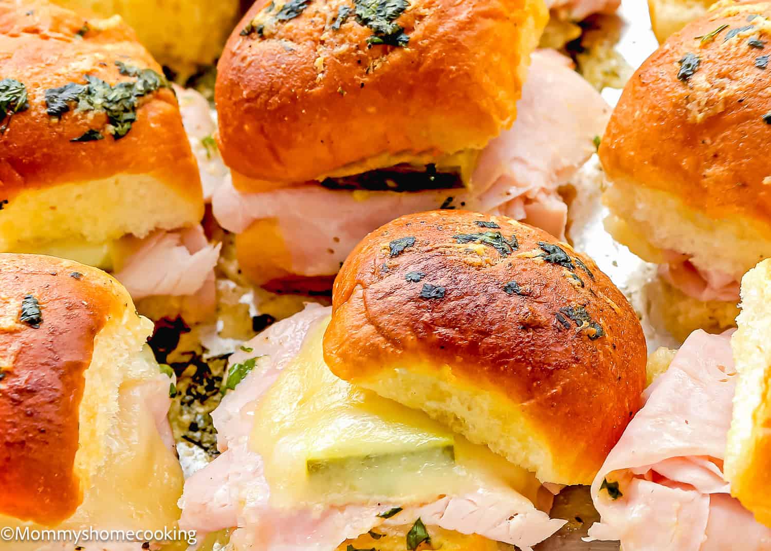 Close-up of easy Cuban sliders made with golden buns topped with herbs, filled with sliced deli turkey and cheese. Ready in 30 minutes!.