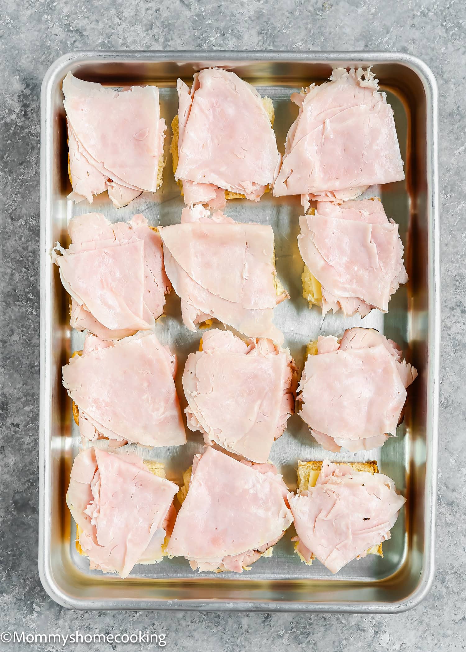 Easy Cuban Sliders ready in just 30 minutes feature sliced ham on small bread squares, perfectly arranged in a metal baking tray.