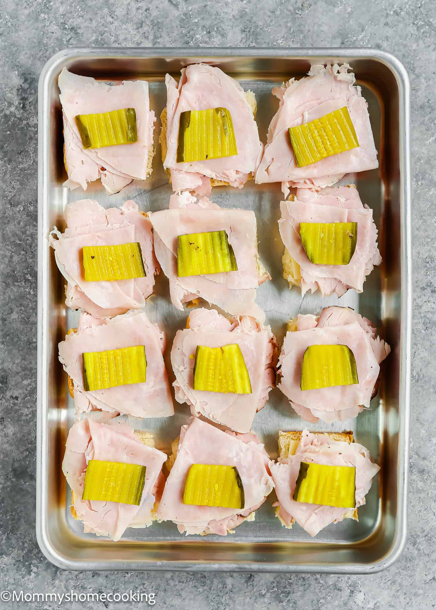 Enjoy these Easy Cuban Sliders: twelve open-faced sandwiches with ham slices and pickles on top, arranged neatly on a baking tray. Ready in just 30 minutes!.