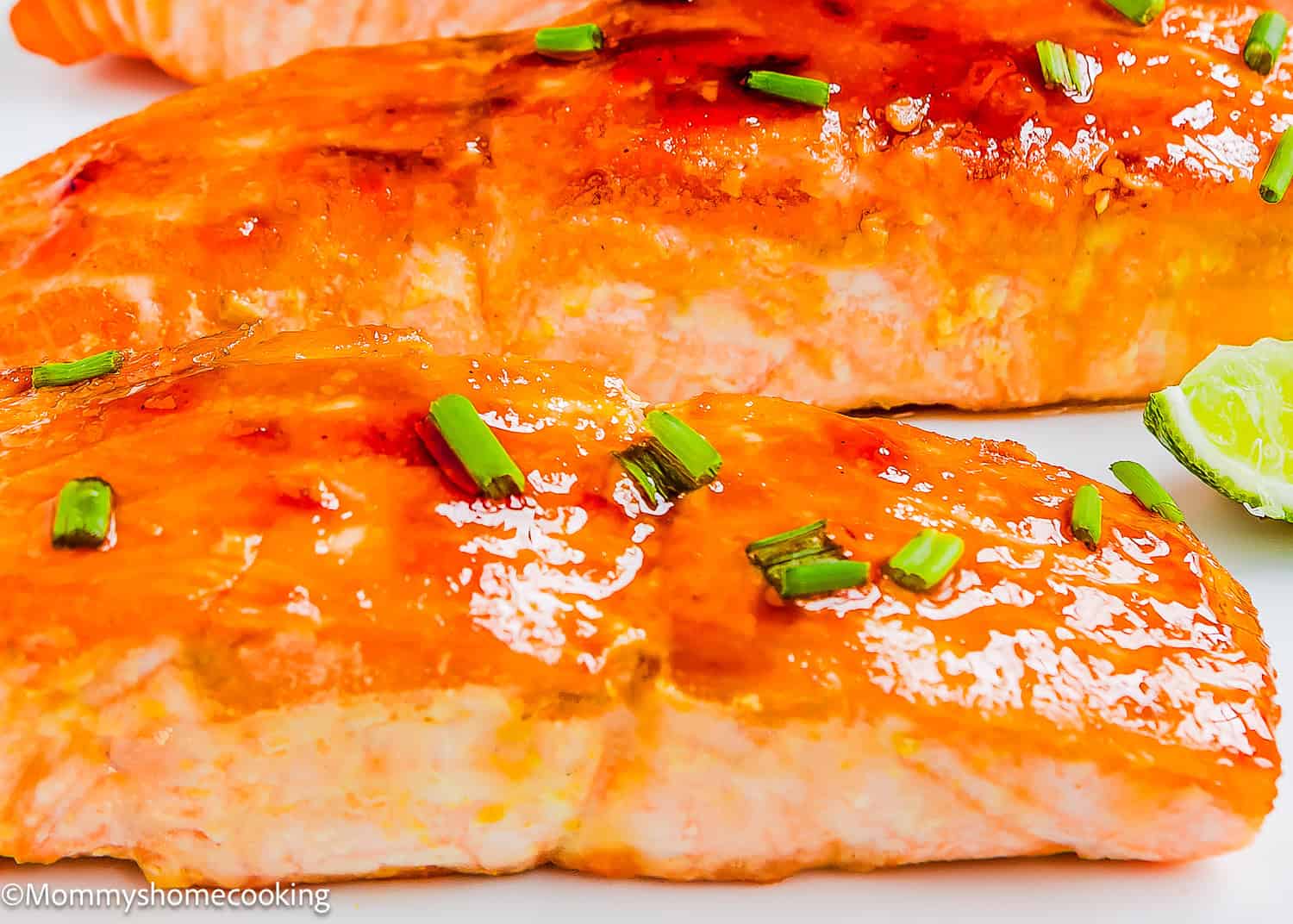 Close-up of Easy Glazed Salmon fillets garnished with chopped chives, with a lime wedge visible on the side.