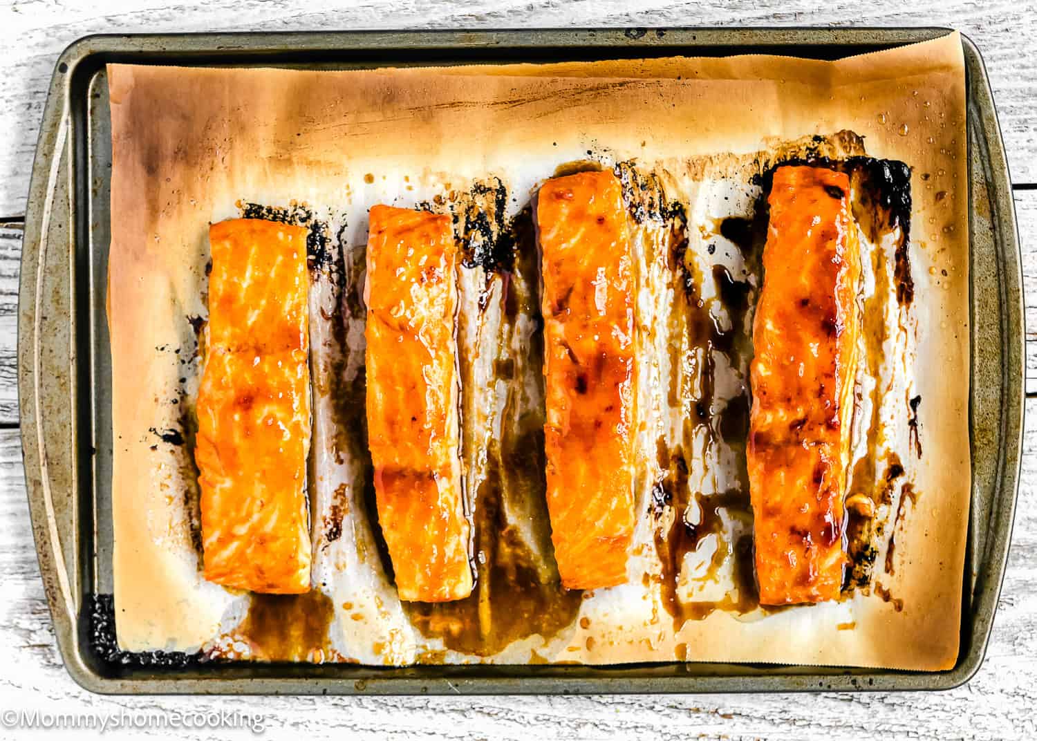 Four Easy Glazed Salmon fillets on a parchment-lined baking sheet, cooked until slightly caramelized and golden, viewed from above.