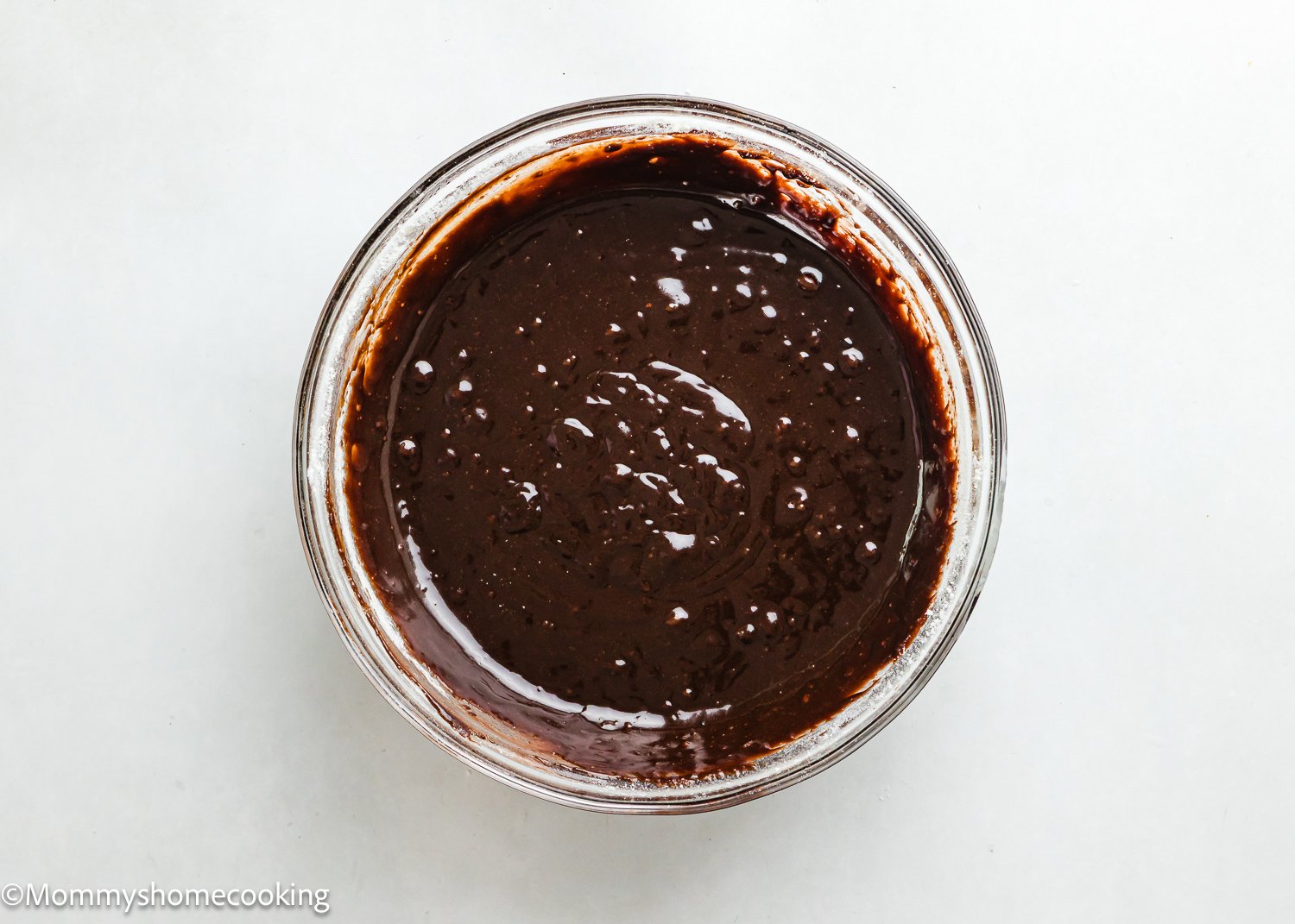 A glass bowl filled with smooth, eggless chocolate batter to make brownies. 