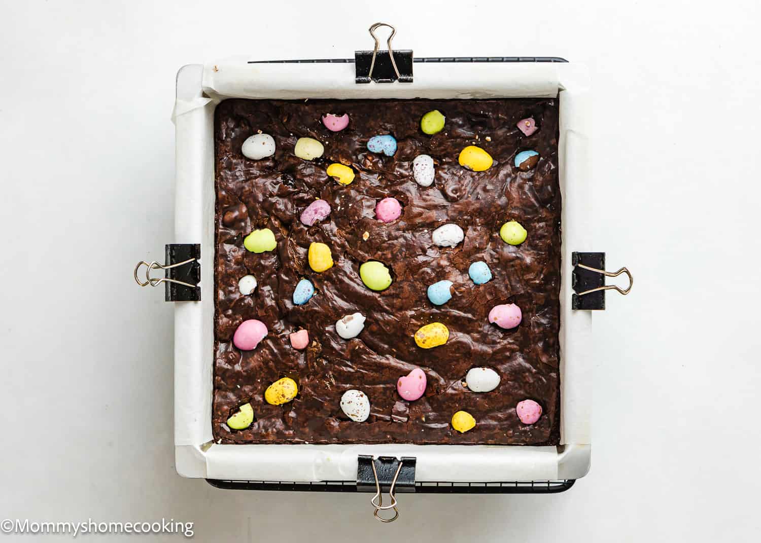 A square pan filled with eggless Cadbury Mini Egg brownies, topped with colorful, egg-shaped candies.