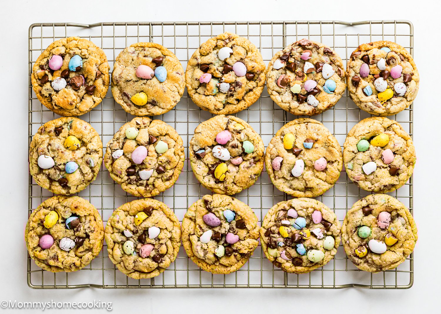 Fifteen eggless cookies with chocolate chips and Cadbury Mini Eggs cool on a wire rack.