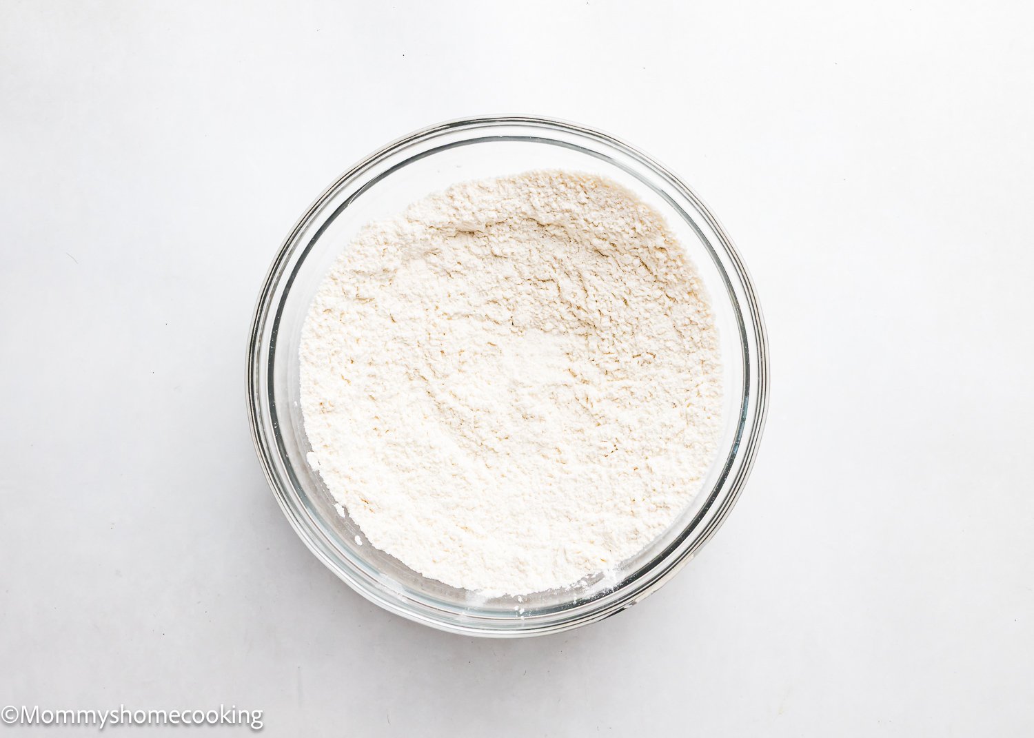 A clear glass bowl brimming with white flour is set against a simple white background, ready to be transformed into delicious eggless Cadbury Mini Egg cookies.