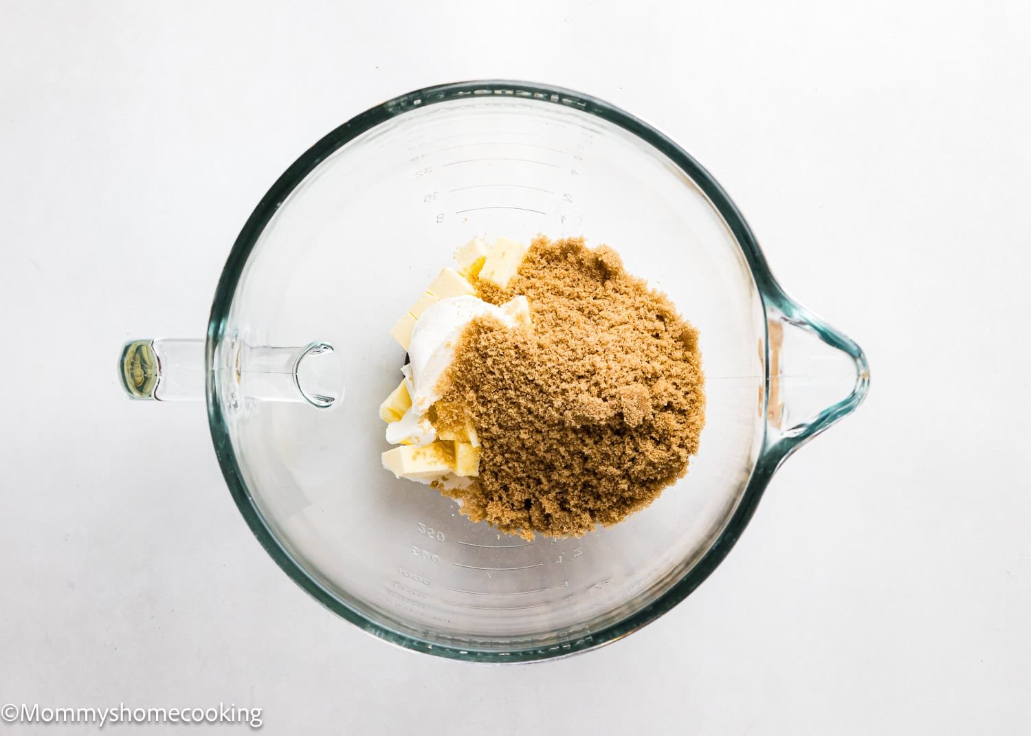 A glass bowl on a white surface holds butter, cream cheese, and brown sugar, ready to make Eggless Cadbury Mini Egg Cookies.