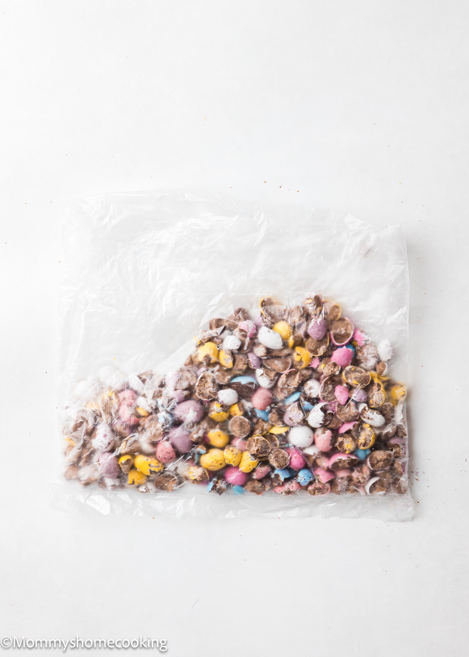 A clear plastic bag filled with colorful, crushed chocolate eggs on a white background, perfect for baking delightful Eggless Cadbury Mini Egg Cookies.