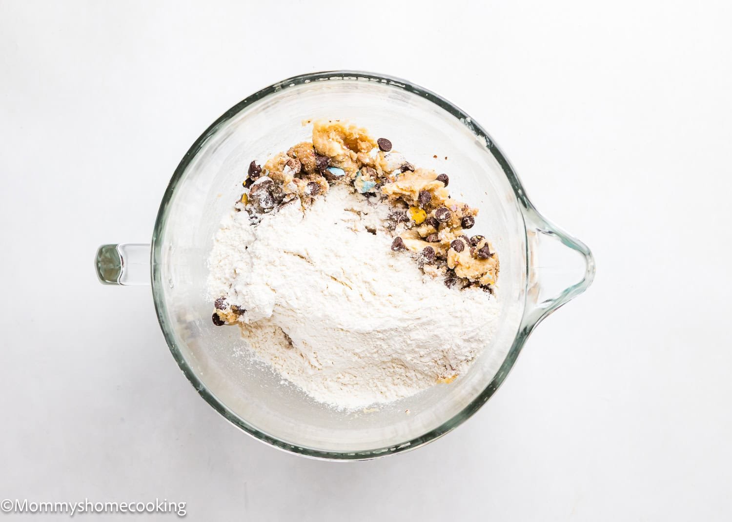 A bowl brimming with flour mixed with chocolate chips, nuts, and colorful candies on a white backdrop. Imagine creating eggless Cadbury Mini Egg cookies with this delightful blend.