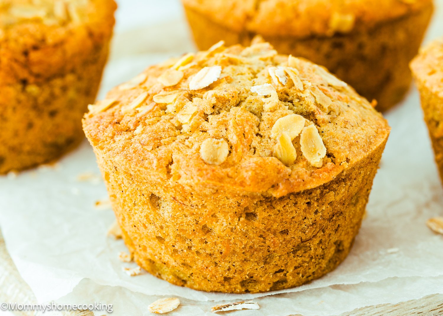Close-up of eggless carrot banana muffins on parchment paper, with a golden-brown crust and oats sprinkled on top.