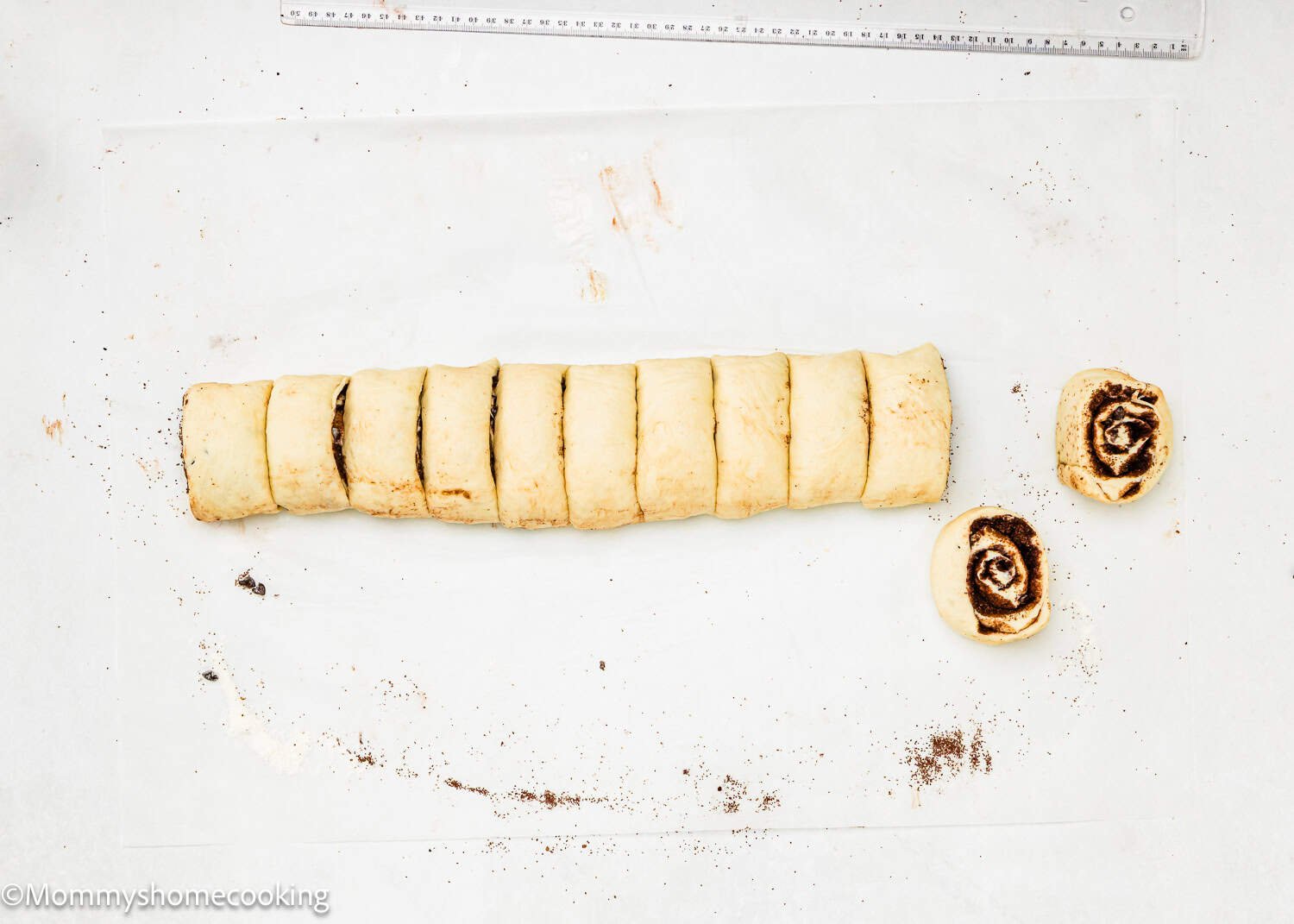 Sliced Eggless Chocolate Cinnamon Rolls dough on a floured surface, with two pieces separated from the rest of the roll.