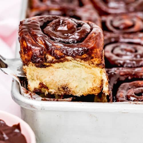 A tray of Eggless Chocolate Cinnamon Rolls with one roll being lifted out, exposing its soft, fluffy interior.