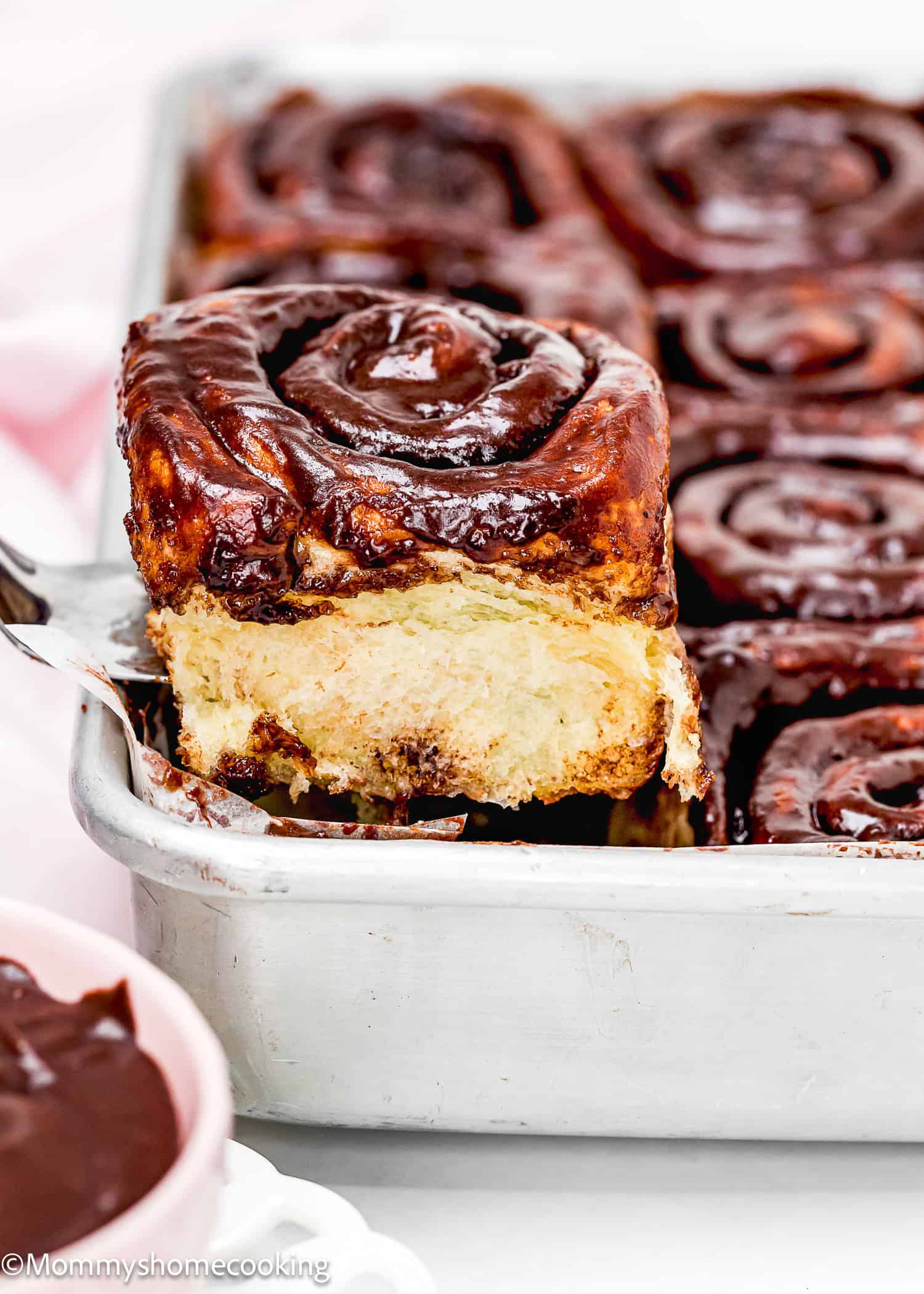A tray of Eggless Chocolate Cinnamon Rolls with one roll being lifted out, exposing its soft, fluffy interior.